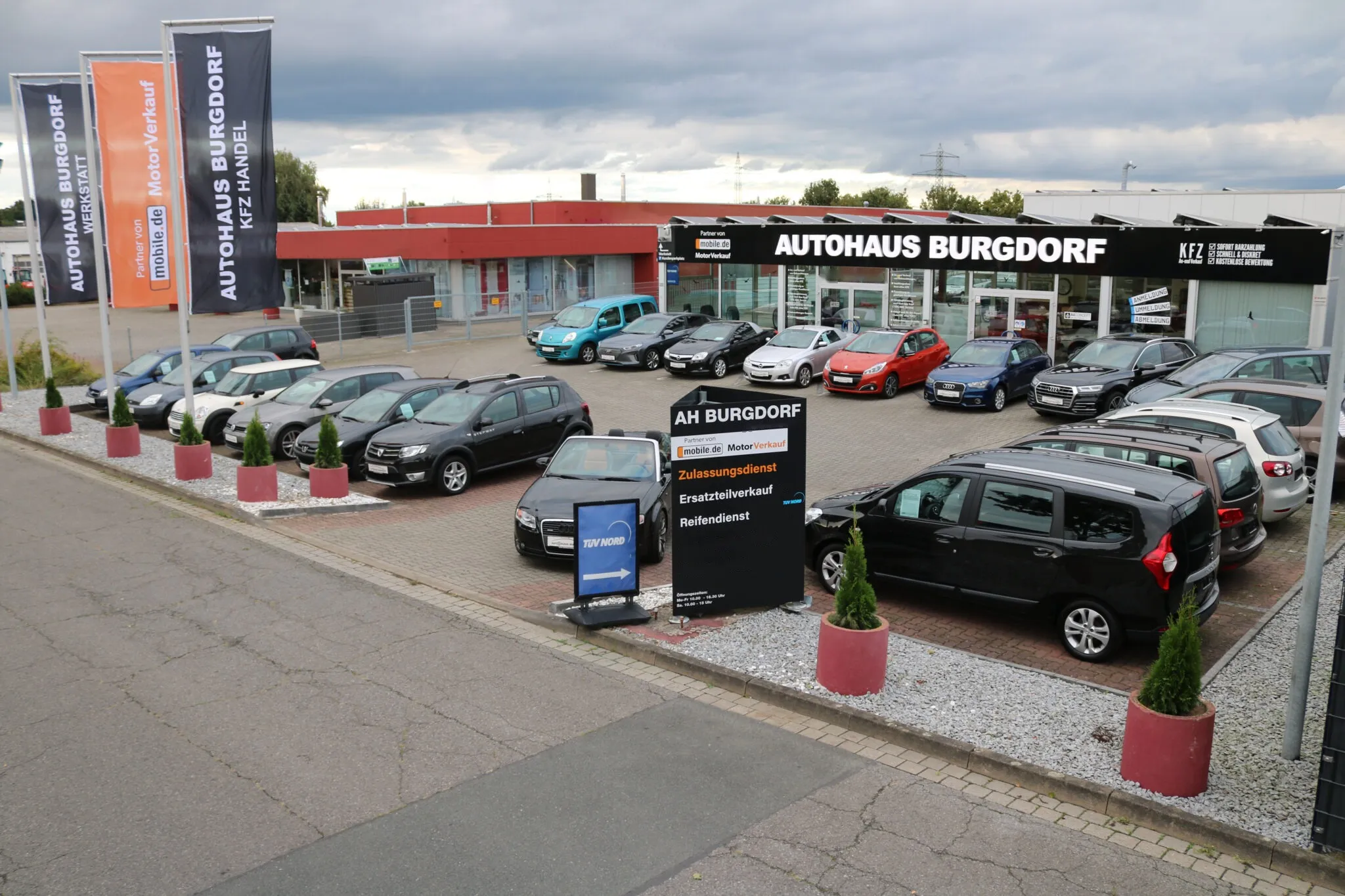 Der Hof des Autohaus Burgdorf mit Fahrzeugen, Fahnen und der Beschilderung am Gebäude